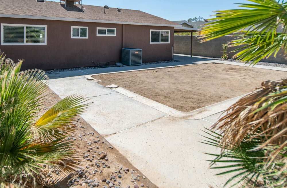 Backyard view featuring a house with a concrete driveway and surrounding landscaping, highlighting the potential for exterior cleaning services like pressure washing and home enhancement.