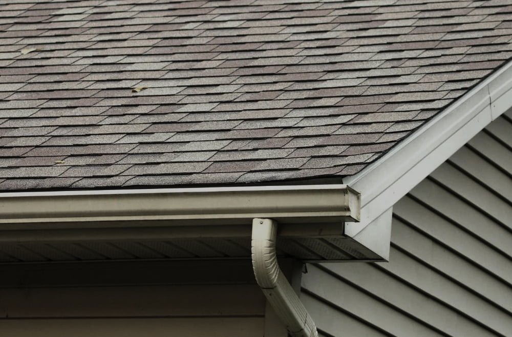 Roof shingles and gutter system, highlighting the importance of gutter cleaning for maintaining exterior property integrity.