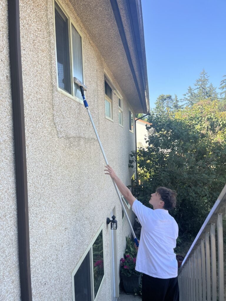 Frater Exterior Cleaning Services employee using an extended pole with a brush for window cleaning in Victoria and Saanich - Frater Exterior Cleaning Services on Vancouver Island specializes in Roof Moss Removal and Treatment, Gutter Cleaning, Window Cleaning, Pressure Washing, House Washing as well as Commercial Exterior Cleaning Services.