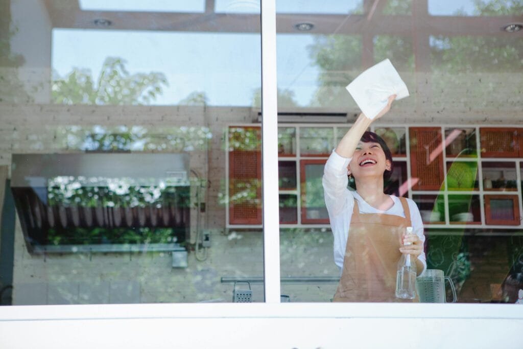 Smiling Victoria BC homeowner wiping kitchen window after professional cleaning service