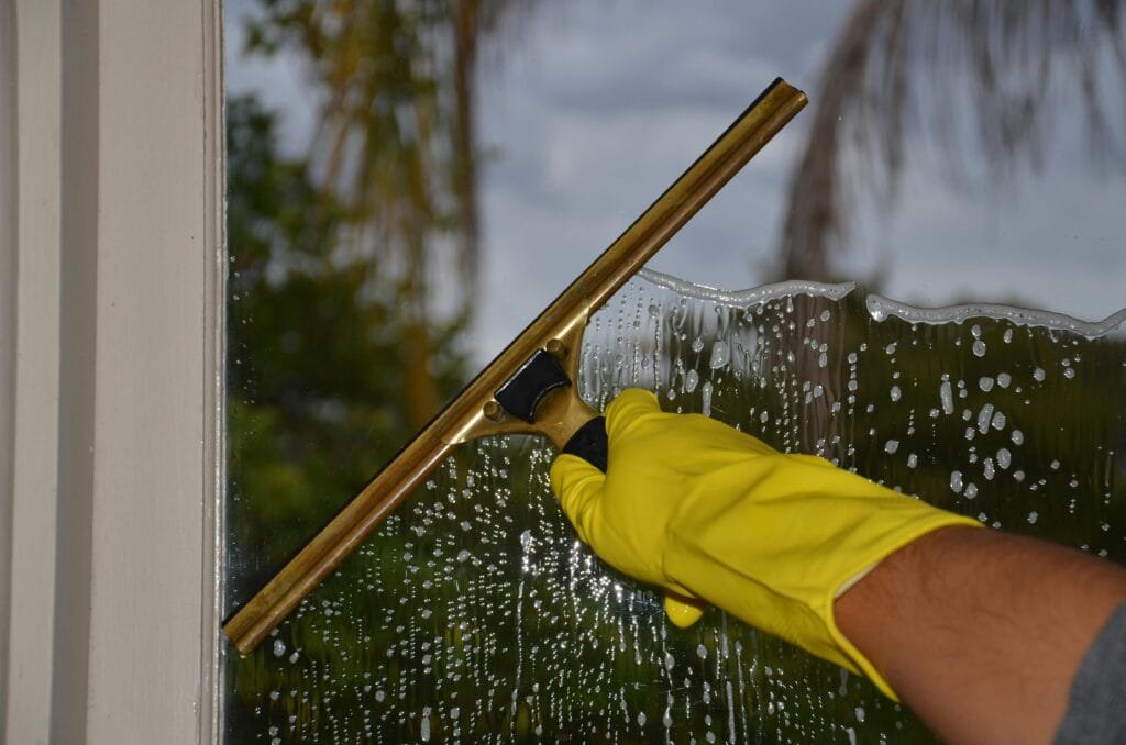 Yellow‑gloved hand using brass squeegee to remove soapy water during Victoria BC window cleaning
